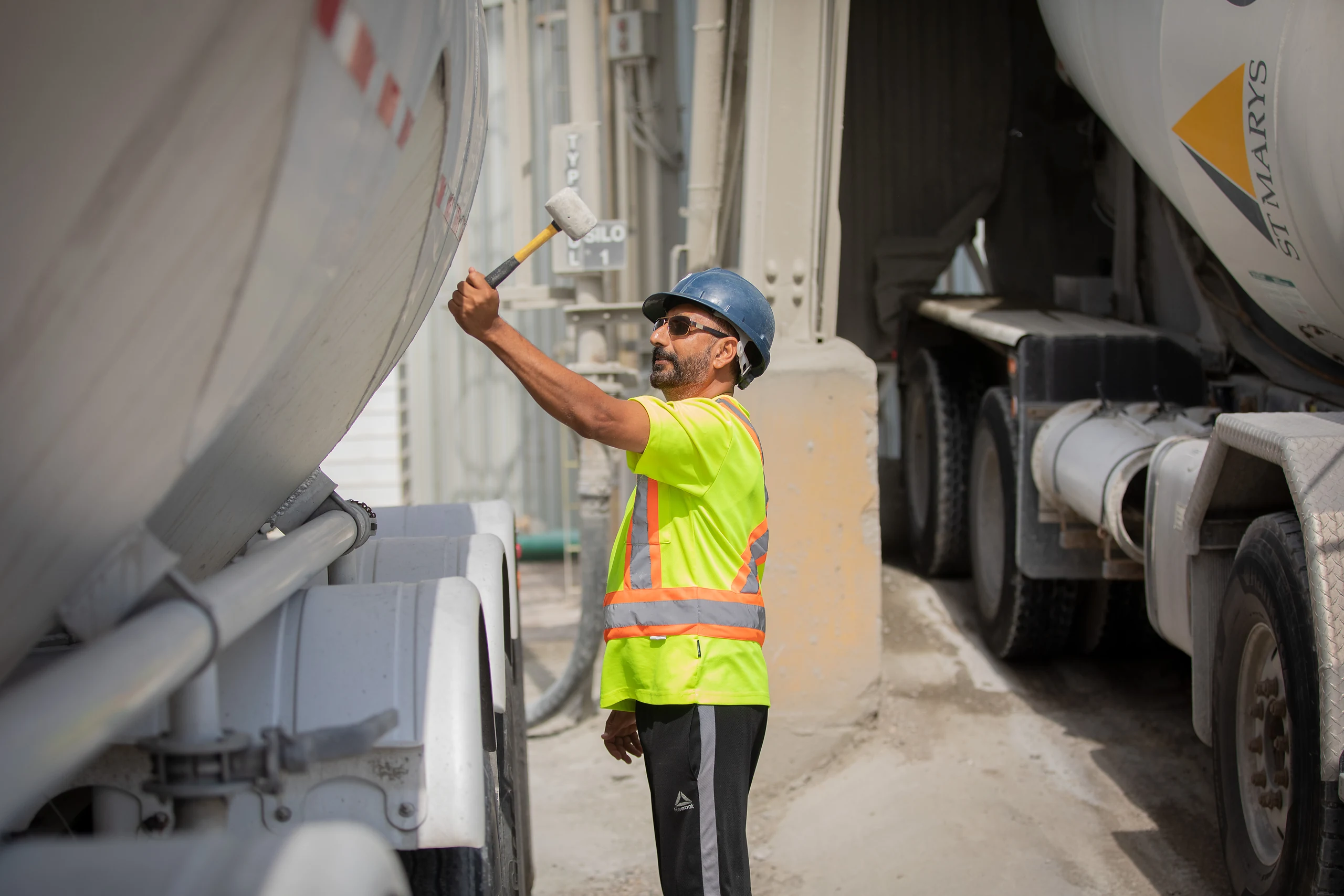 DelaySet - worker in a hi-vis shirt and hard hat beside ready-mix trucks at a plant