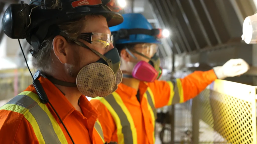 Canada Building Materials Careers - two plant workers in respirators, hard hats and hi-vis gear at work